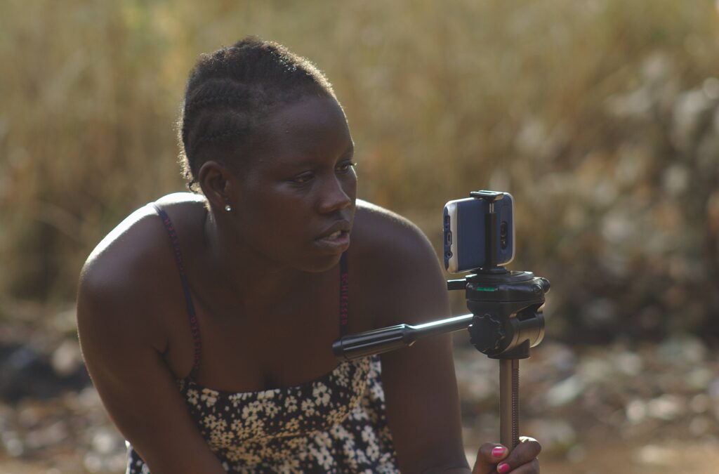 A young African woman leans as she looks into a phone camera which is on a tripod 