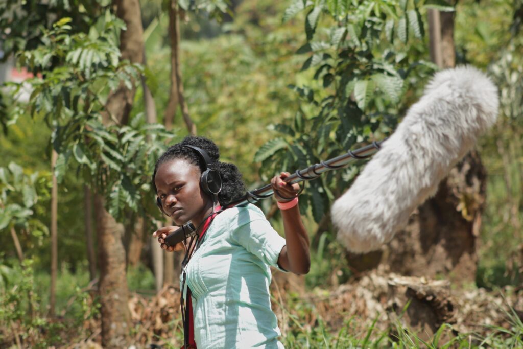 A young woman holding a boom pole, with the 'dead cat' windshied in the foreground.