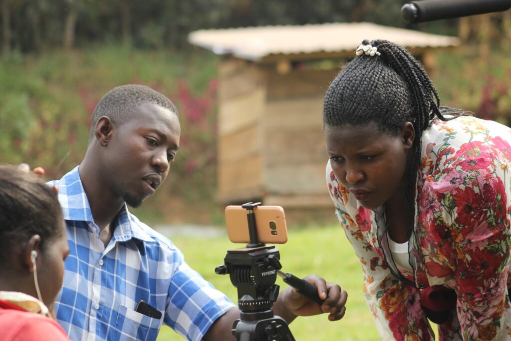 a man and a woman staring at a smart phone mounted on a tripod, which is between them.