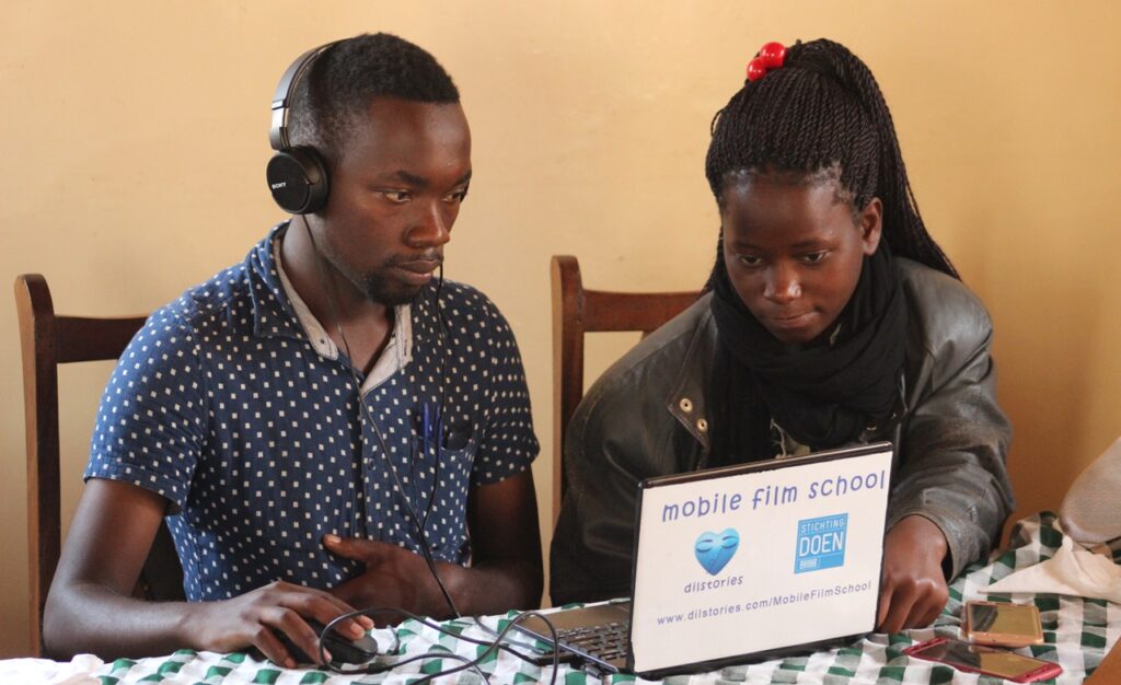 A man and a woman sit behind a laptop, editing a film