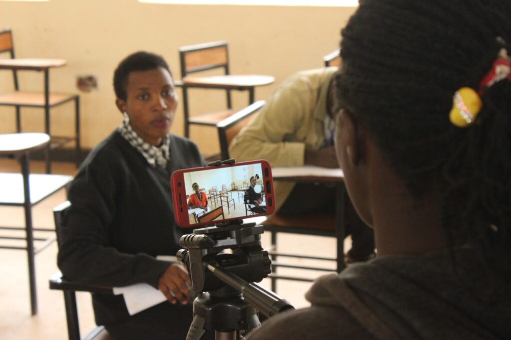 Close up of a smart phone on a tripod filming a movie scene of a woman sitting on a school desk in a classroom