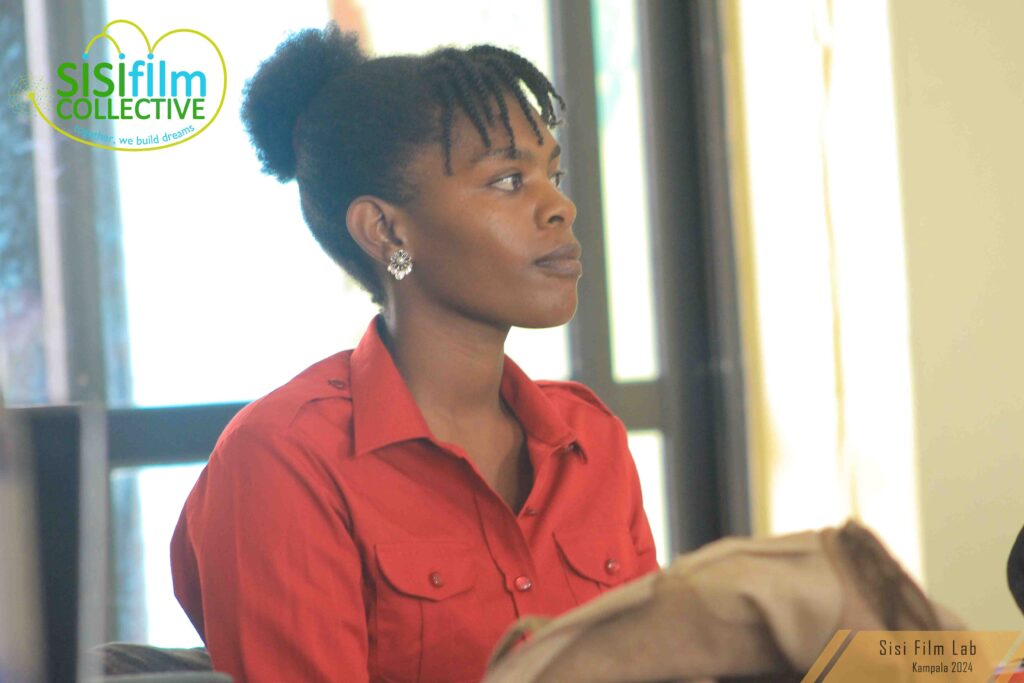 A black African woman with African natural hair twisted at the front is dressed in a red blouse is attentively listening to what ever is going on where she is.