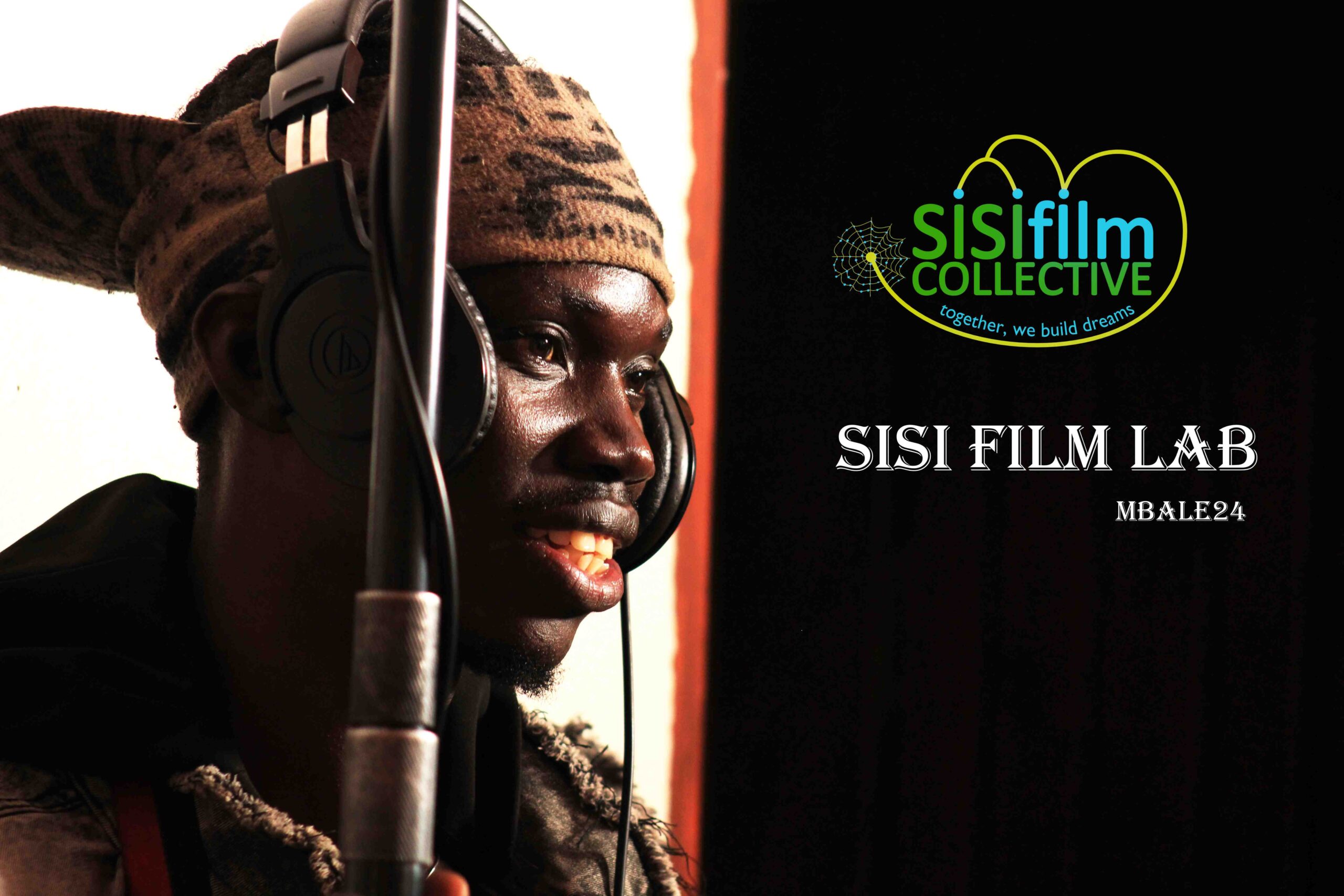 young African man wearing headphones and holding a boom is smiling.