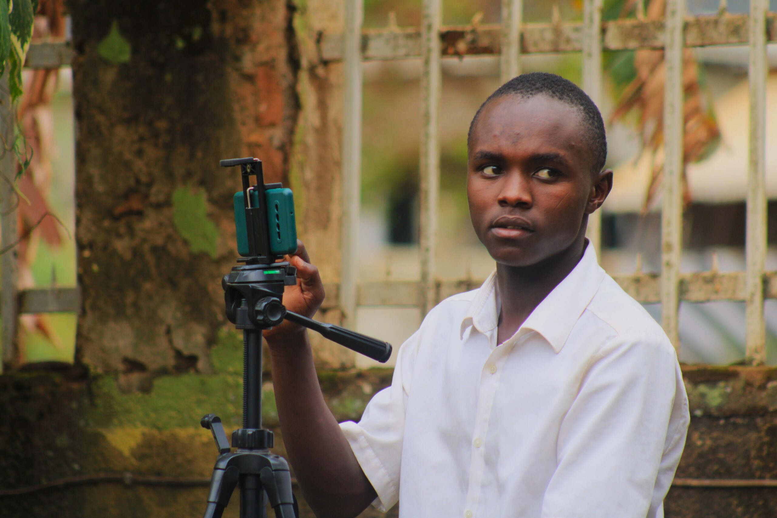 A young boy dressed in a white shirt is operating a phone on a tripod, shooting something.