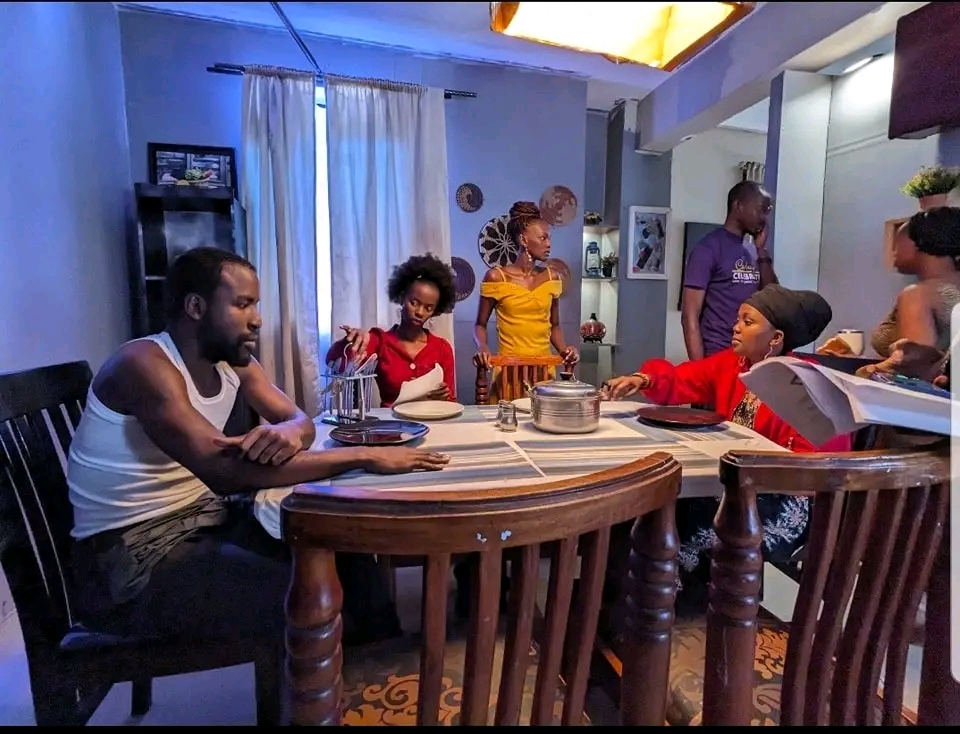 Anumber of young men and women. Others sit at the dining table while some stand. The lighting is cinematic.
