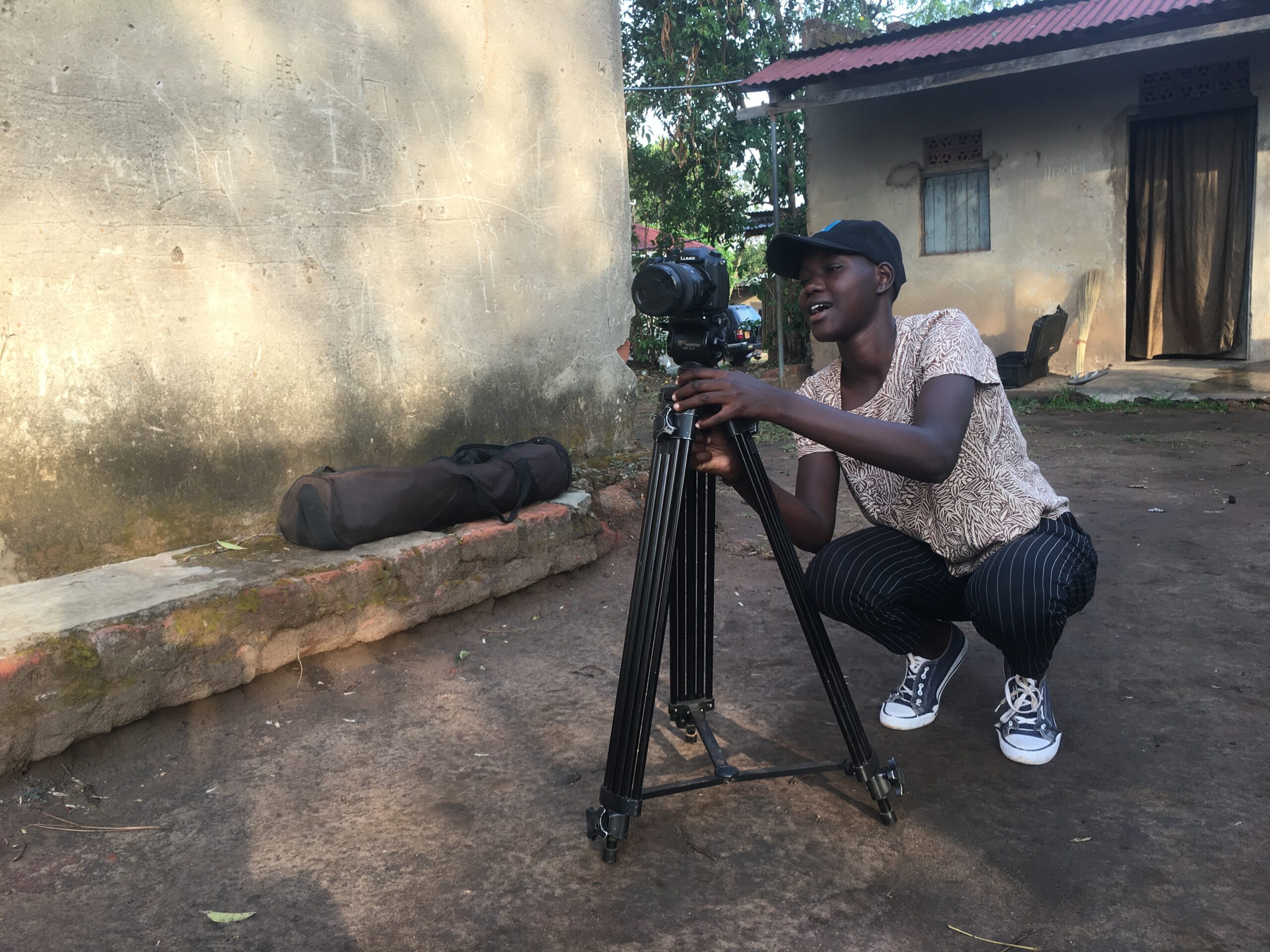 A young woman is operating a camera on a tripod. She squats as her hands adjust it.