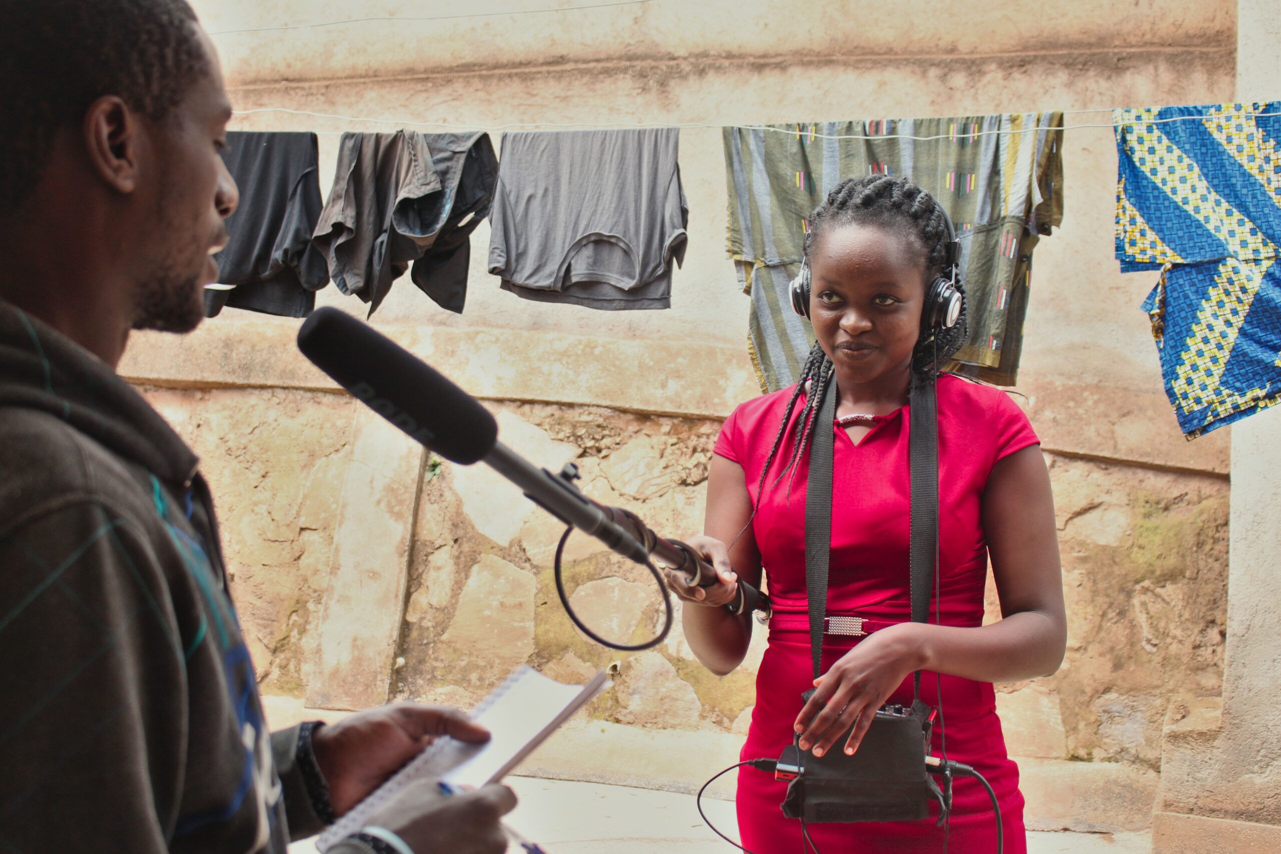 A young lady carrying a boom and wearing headphones is recording sound.