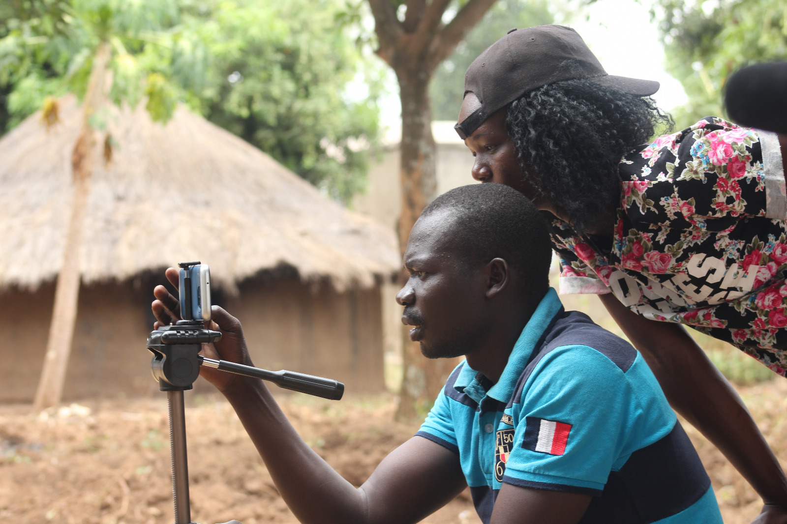 A young man and a woman are looking at a smartphone mounted on a tripod.